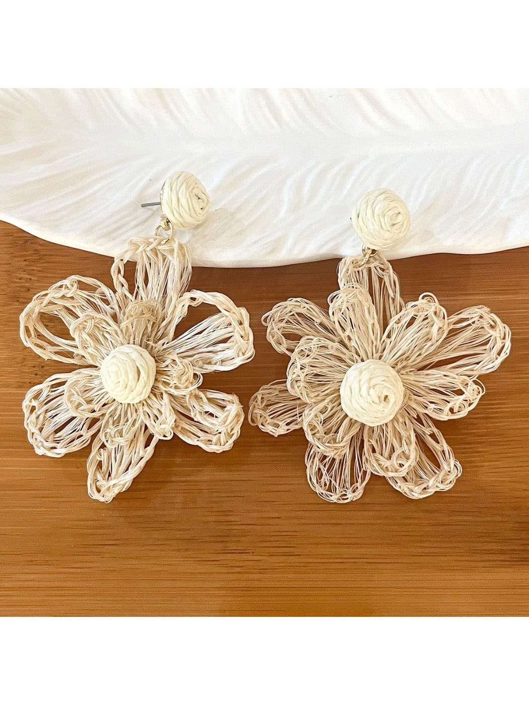 Earedge raffia flower shaped drop earrings displayed on wooden surface