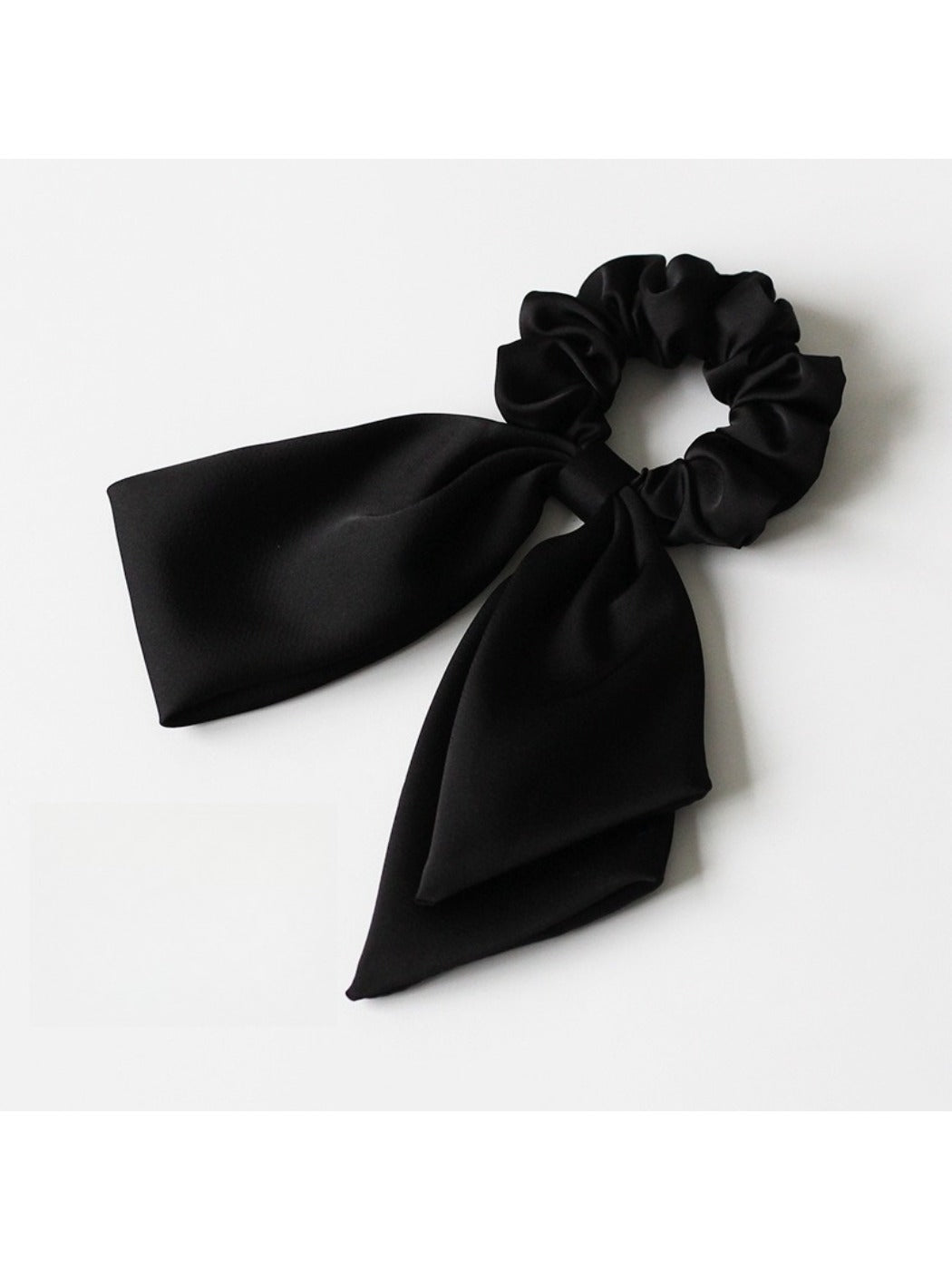 Satin bow hair tie in soft pink color placed next to matching satin ribbon