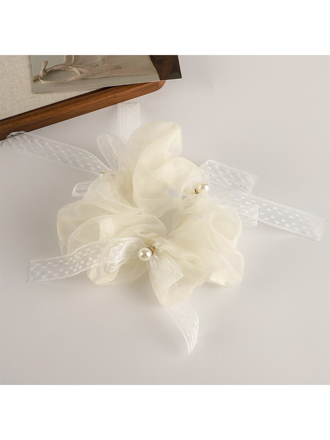Gifty ruched scrunchie in soft pink fabric with bow accent on a wooden surface