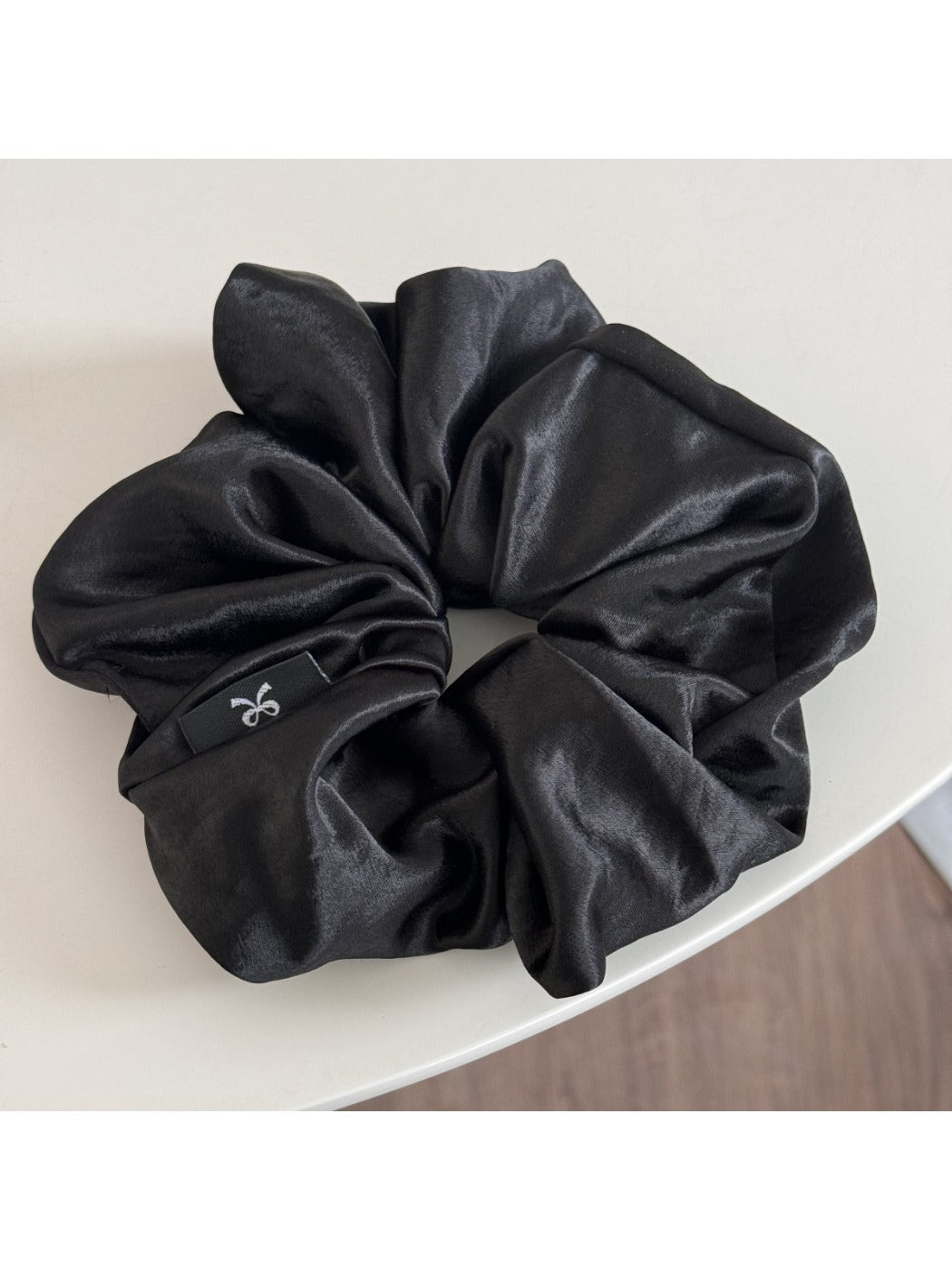 Glossy satin scrunchie in pink coiled loosely on a white surface