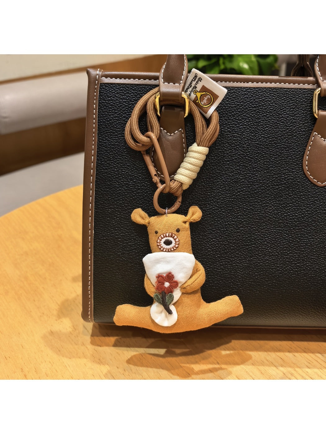 Bear keychain with a smiling expression holding a pink flower close-up