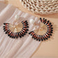 Pink and black raffia woven earrings hanging from gold-tone hoops