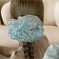 Beige satin scrunchie with ruched texture displayed on a flat surface