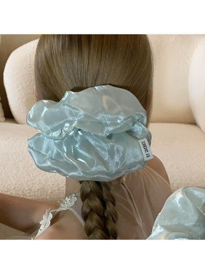 Beige satin scrunchie with ruched texture displayed on a flat surface