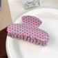 Beau pink hair claw clip with white polka dots placed on a wooden surface