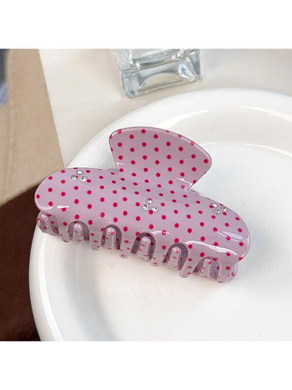 Beau pink hair claw clip with white polka dots placed on a wooden surface