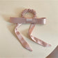 Close-up of a stylish hair tie with a large bow embellishment in soft pink fabric