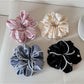 Close-up of Gifty satin scrunchie in soft pink fabric with smooth texture