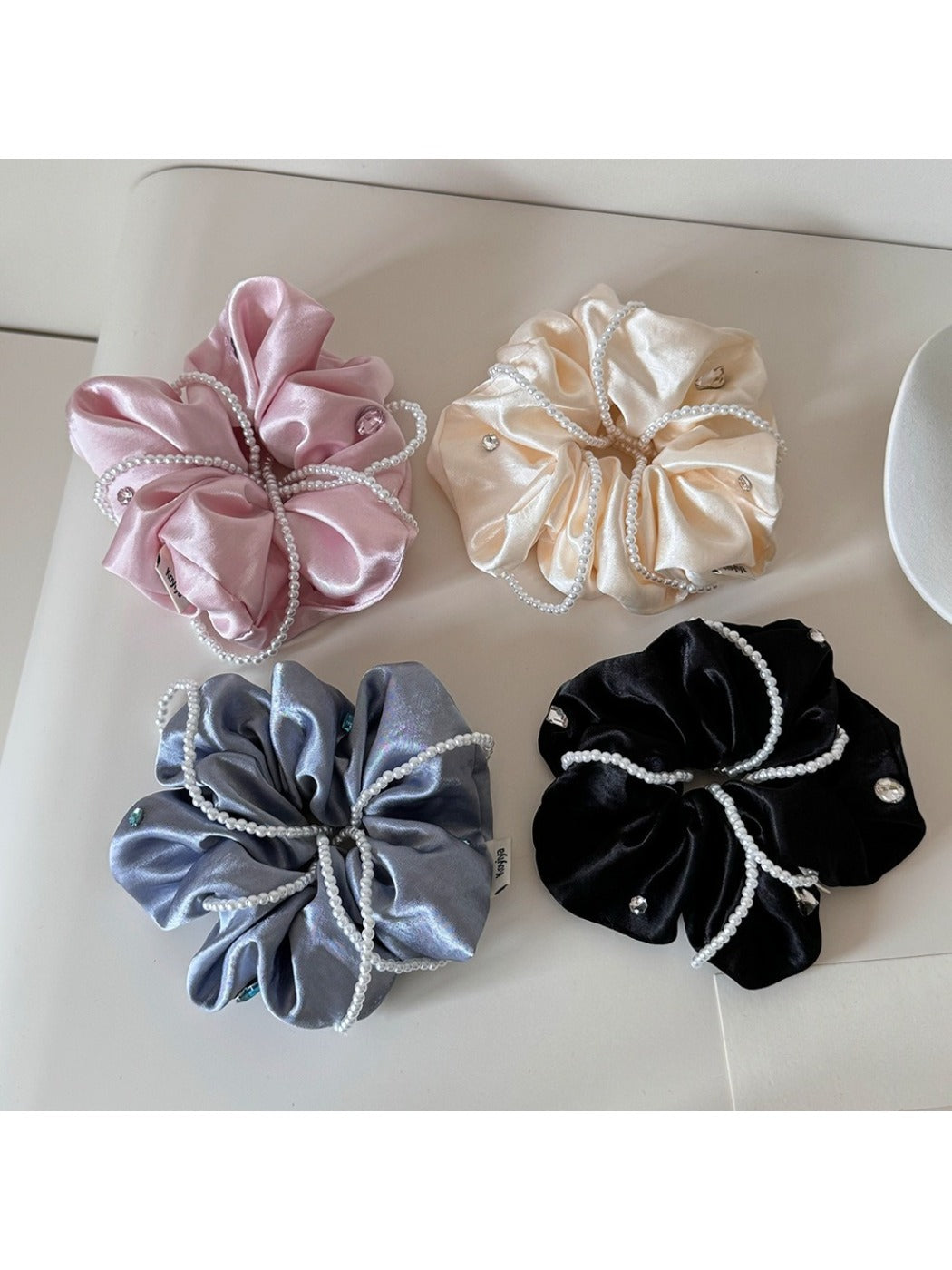 Close-up of Gifty satin scrunchie in soft pink fabric with smooth texture