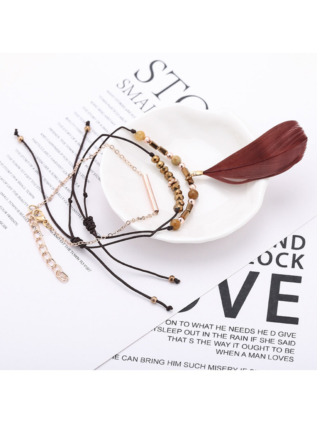 Lovra small bead bracelet with feather pendant laid flat on wooden surface