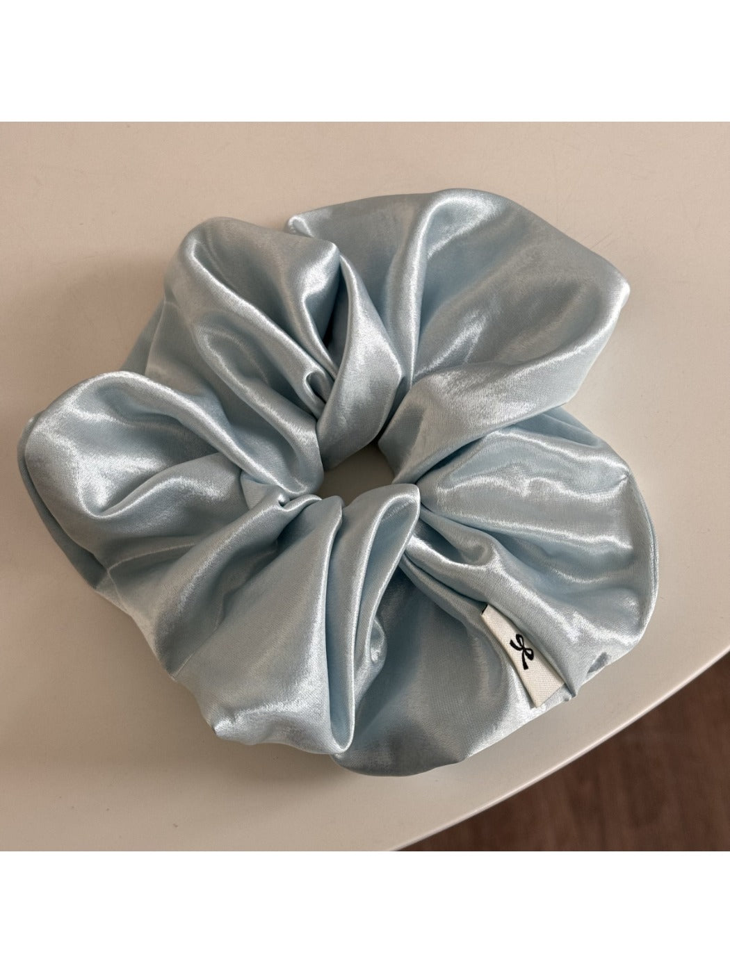 Glossy satin scrunchie in pink displayed flat showing elastic inside
