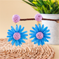 Pair of lightweight raffia stud earrings with daisy flower design on beige fabric