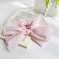 Striped bow scrunchie in beige and white stripes on a neutral background