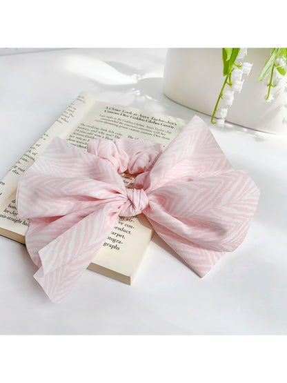 Striped bow scrunchie in beige and white stripes on a neutral background