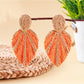 Model wearing Earedge raffia woven leaf shaped earrings with natural makeup