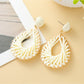 Pair of Earedge hollow drop woven earrings laid flat on wooden surface