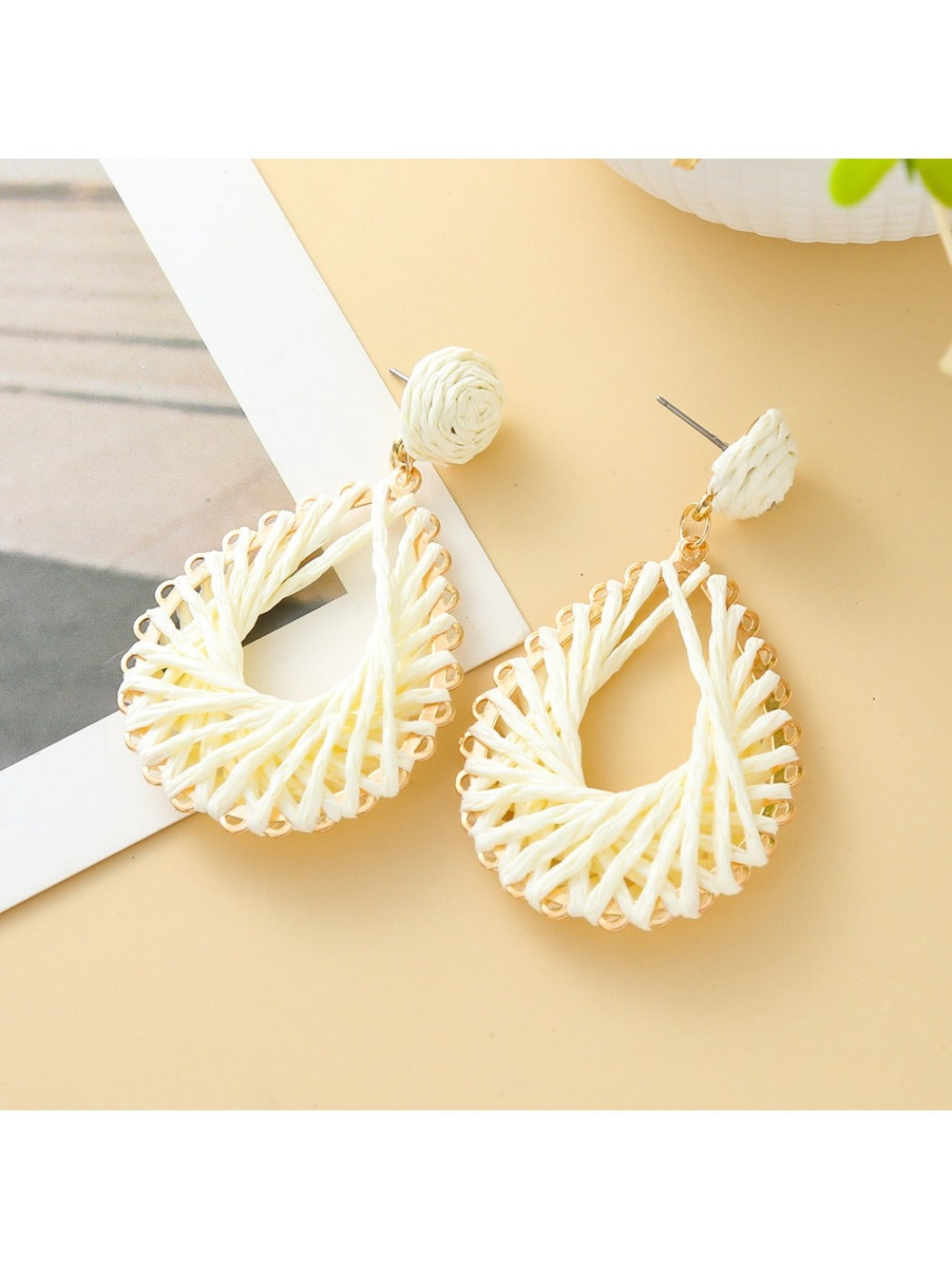 Pair of Earedge hollow drop woven earrings laid flat on wooden surface