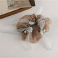 Gifty Sweet Bow Accented Ruched Scrunchie held in hand against neutral background
