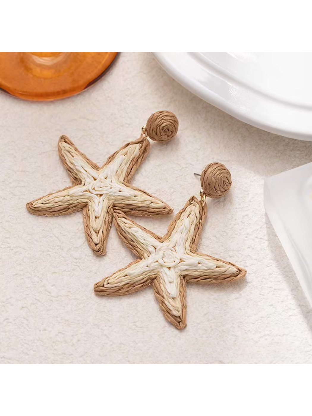 Pair of Earedge Starfish Raffia Woven Stud Earrings displayed on a beige fabric