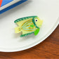 Beau tropical fish shaped hair clip displayed alongside tropical leaves for thematic styling