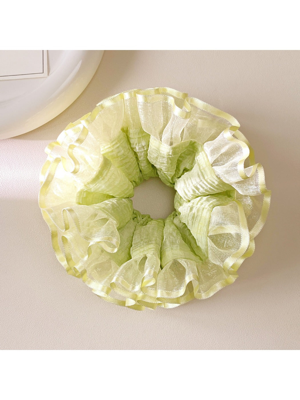 Light green ruffle scrunchie styled on a wrist with soft lighting