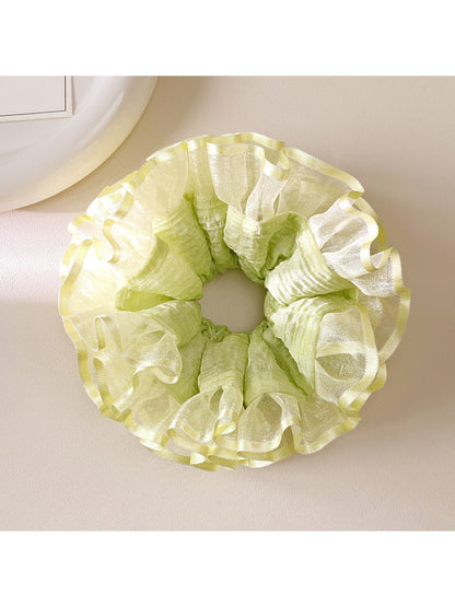 Light green ruffle scrunchie styled on a wrist with soft lighting