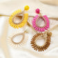 Side view of oval raffia drop earrings showing woven texture and gold hooks