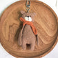 Bear keychain with a red scarf displayed against a pastel background