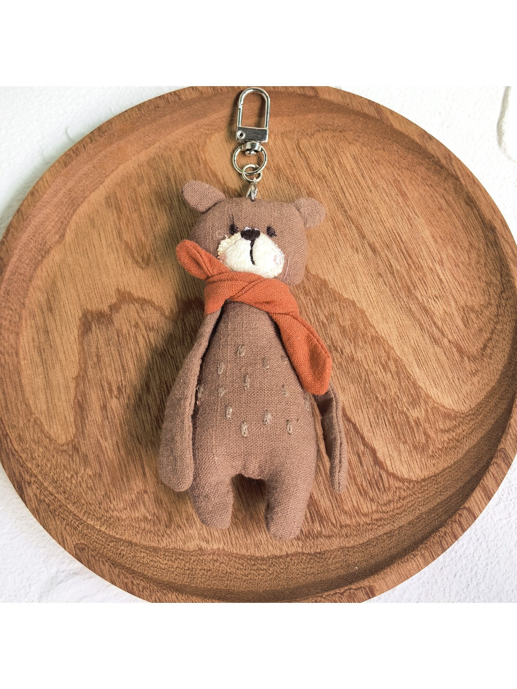 Bear keychain with a red scarf displayed against a pastel background