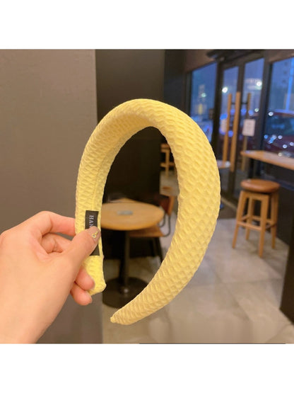 Yellow headband with bow shown from above on a neutral background