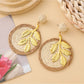 Earedge round leaf pendant earrings resting on a textured fabric