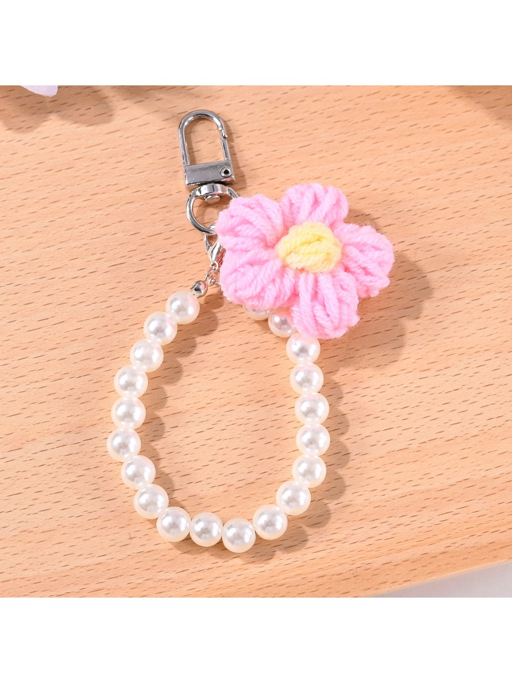 Yarn flower and beaded keychain hanging from a metal ring with a wooden surface background