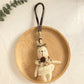 Bunny pendant keychain resting on a fabric surface with a blurred background