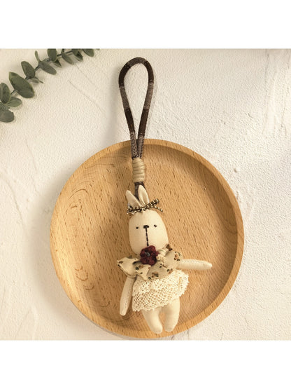 Bunny pendant keychain resting on a fabric surface with a blurred background