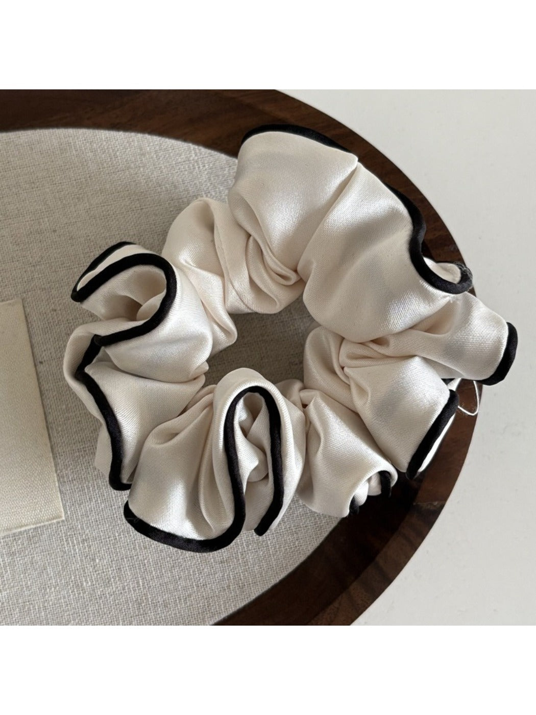 Pink satin scrunchie with ruffled design placed next to matching hairpins