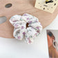 Multiple Gifty floral scrunchies stacked, highlighting ruffled texture and bow accents