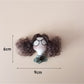 Fabric doll keychain hanging from a metal ring with curly hair and stitched dress