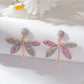 Raffia dragonfly earrings displayed with green leaves background