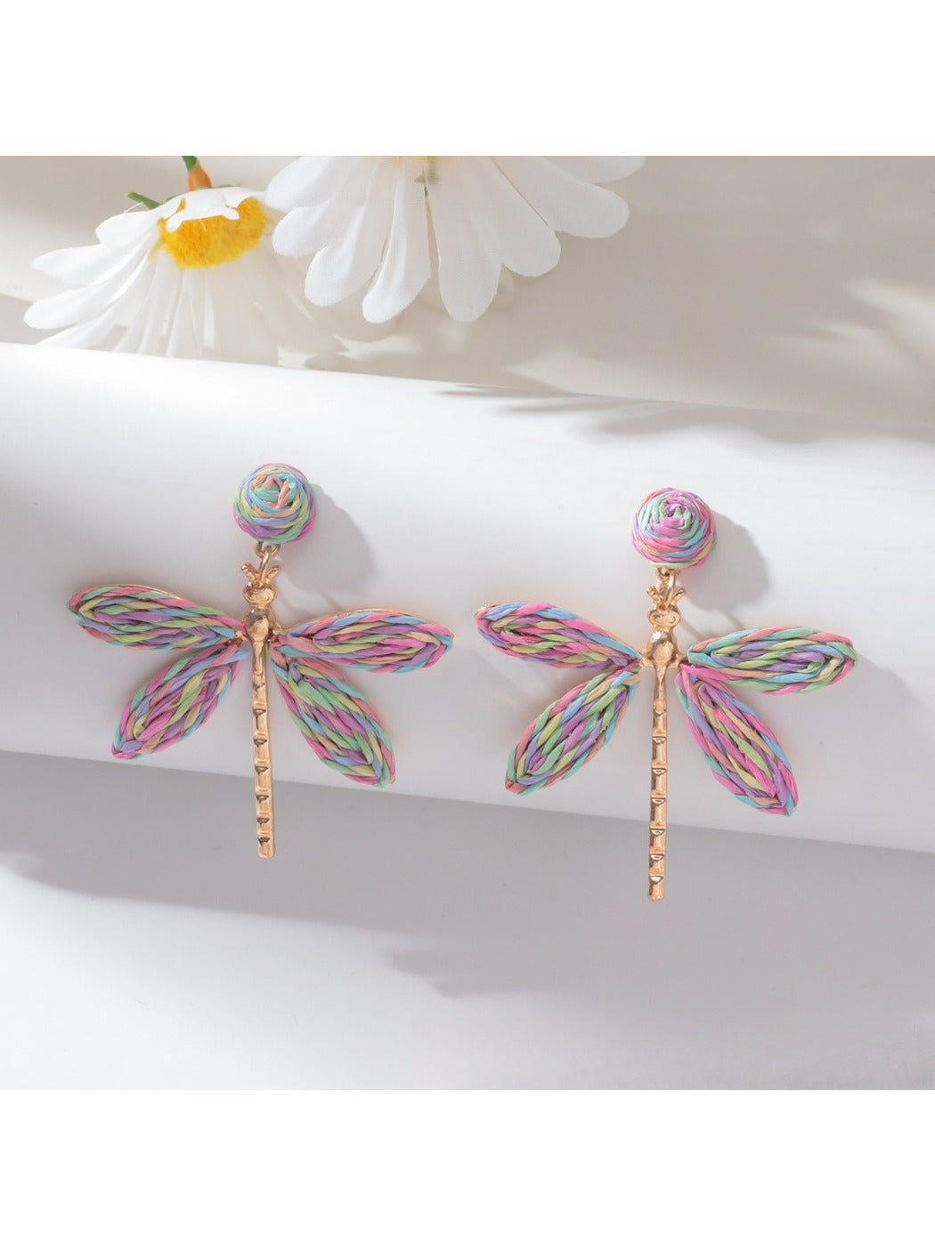 Raffia dragonfly earrings displayed with green leaves background