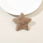 Plush star hair clip clipped onto a light pink fabric surface for display