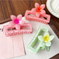 Beau square ombre flower shaped claw clip held in hand displaying size and color gradient