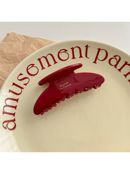 Beau red hair clip positioned on flat surface showing underside clasp mechanism