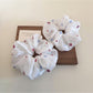 White flower scrunchie styled on a wrist against a neutral background