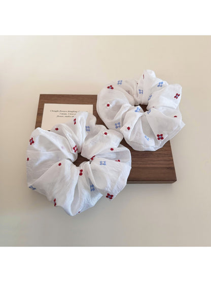 White flower scrunchie styled on a wrist against a neutral background