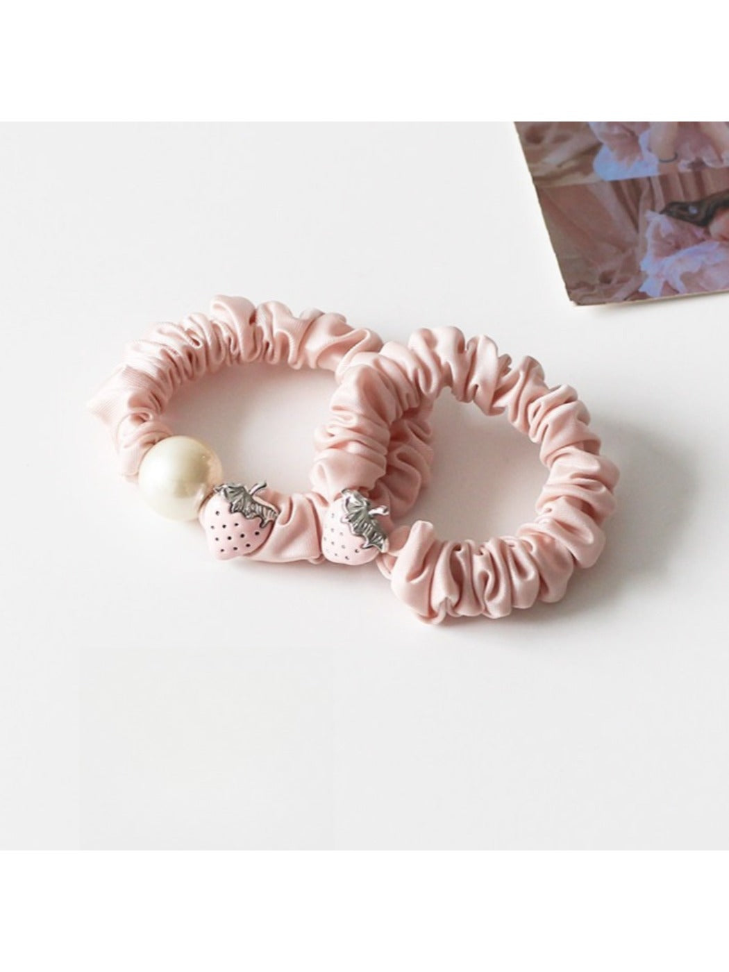 Strawberry hair tie worn on a model's wrist with a blurred background