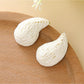 Earedge raffia water drop shaped stud earrings placed next to green leaves