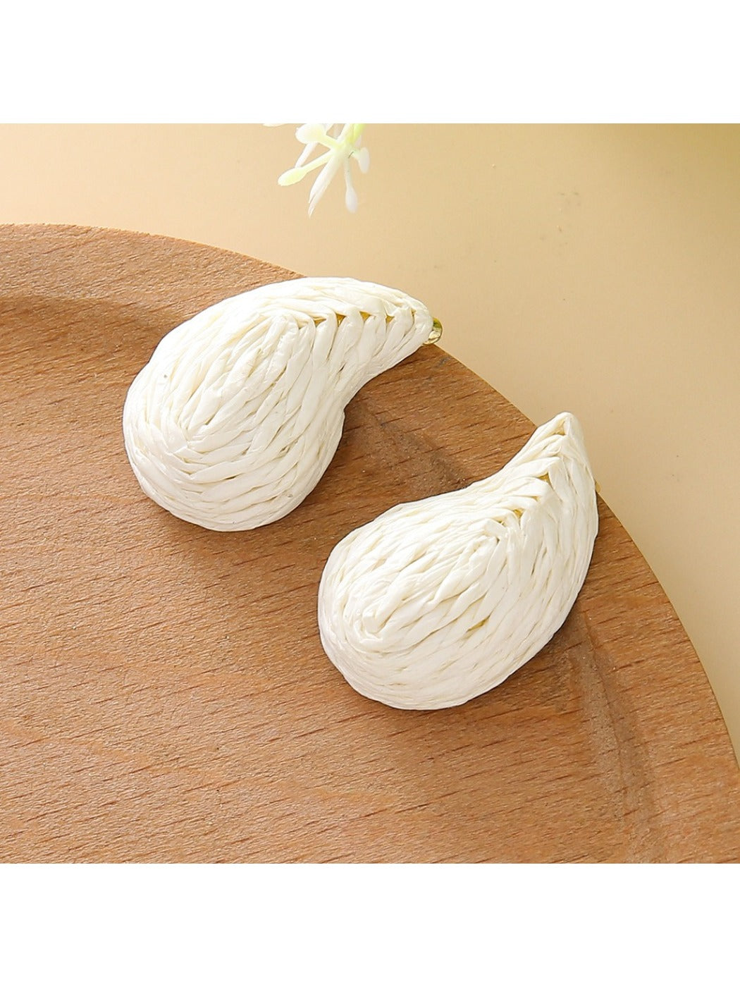 Earedge raffia water drop shaped stud earrings placed next to green leaves