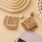 Earedge raffia square earrings displayed on a wooden surface
