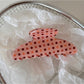 Beau pink acetate hair clip with white polka dots displayed on a wooden surface