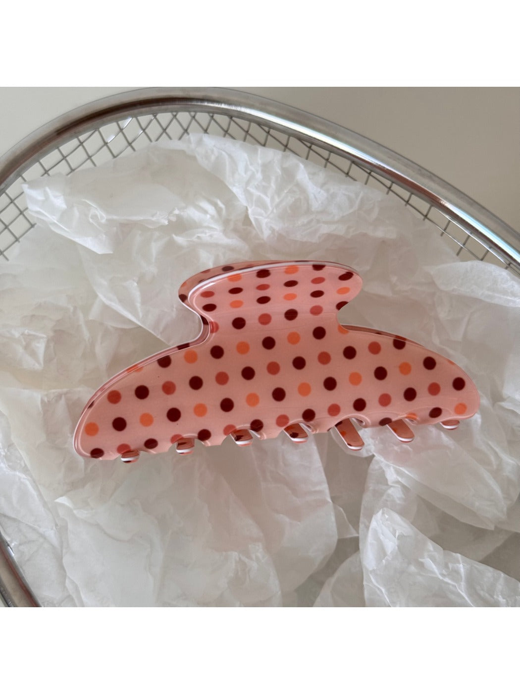 Beau pink acetate hair clip with white polka dots displayed on a wooden surface